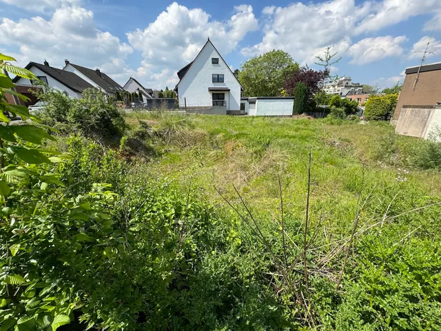 Unbebautes Grundstück mit Wiese, im Hintergrund Wohnhäuser